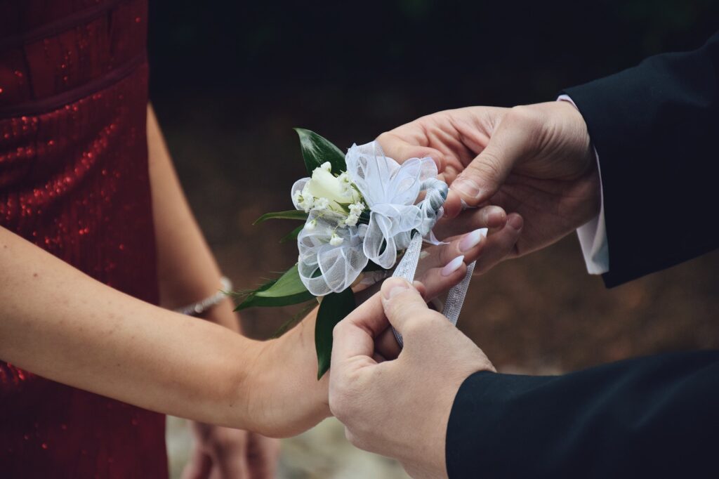 A boy is putting a corsage on girls wrist. Couples at a special event